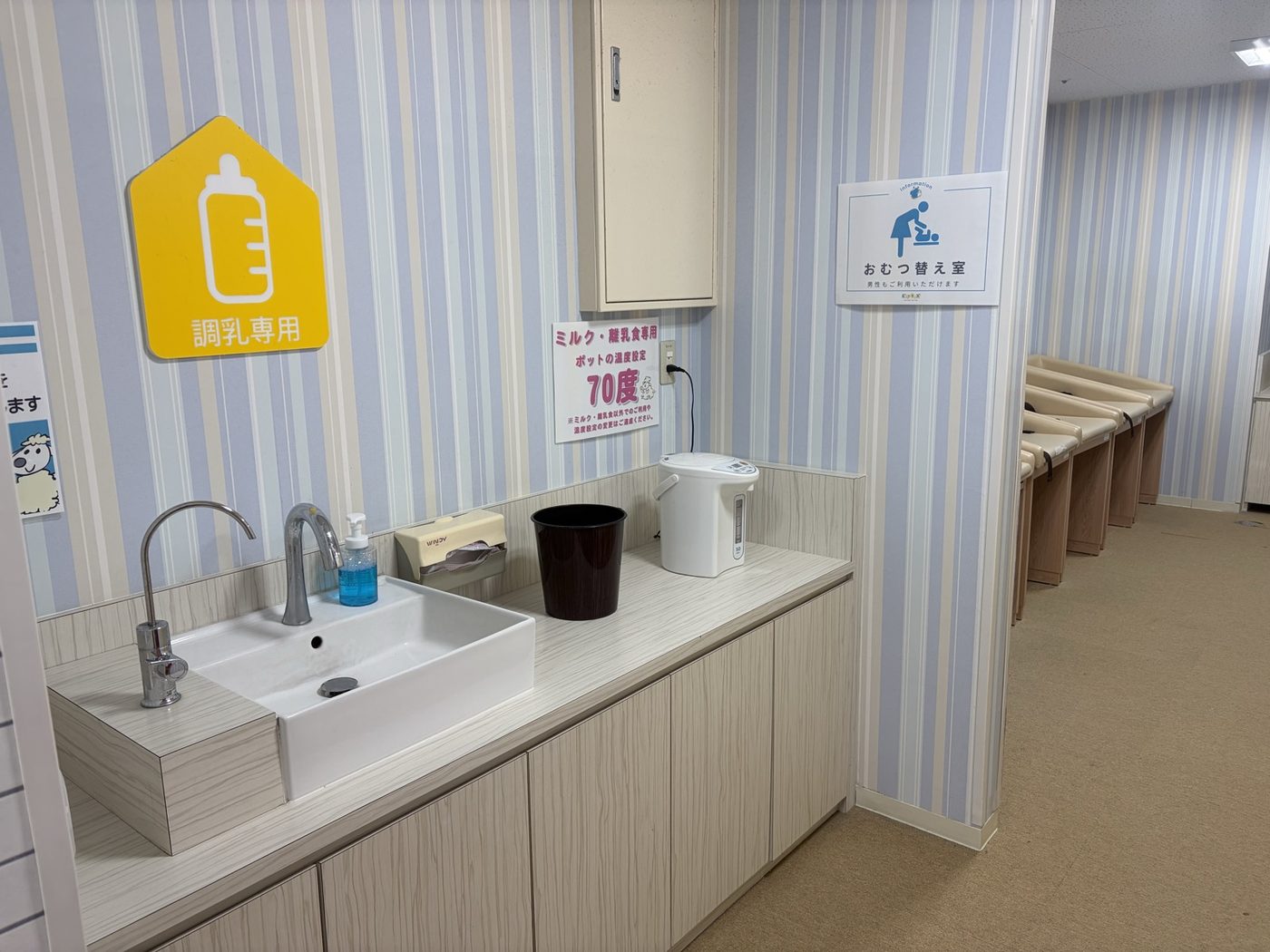 ピュアハートキッズランド ポンテポルタ千住店の調乳スペース。「調乳専用」の表示とシンク、ポットが置かれ、奥に「おむつ替え室 男性もご利用いただけます」の案内とおむつ替え台が並ぶ
