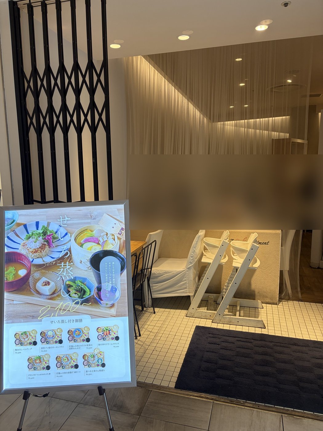 24/7 cafe apartment 有楽町の入口。ハイチェア型のベビーチェアが2台並び、手前にせいろ蒸しのメニュー看板が立っている