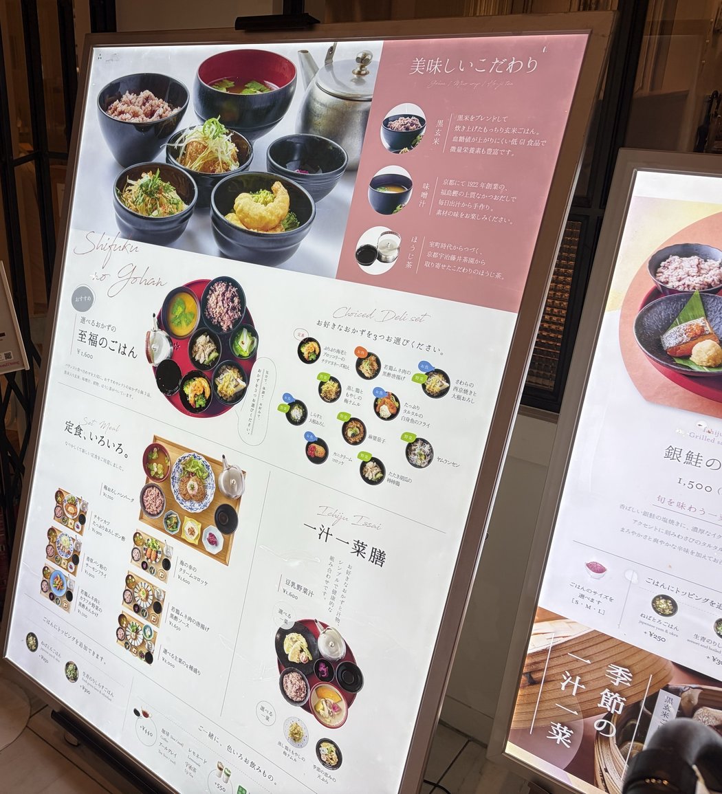 24/7 cafe apartment 有楽町の店頭のメニュー看板。選べるおかずの至福のごはん1,600円と、小鉢のおかずの一覧